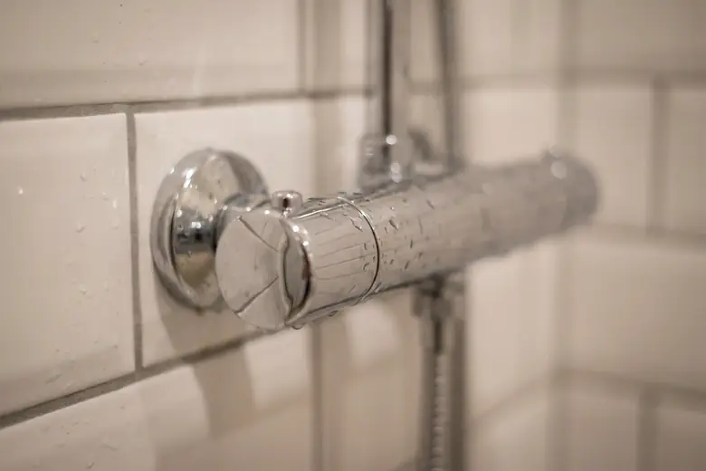 Détail d’un mitigeur thermostatique chromé posé sur une paroi carrelée de douche